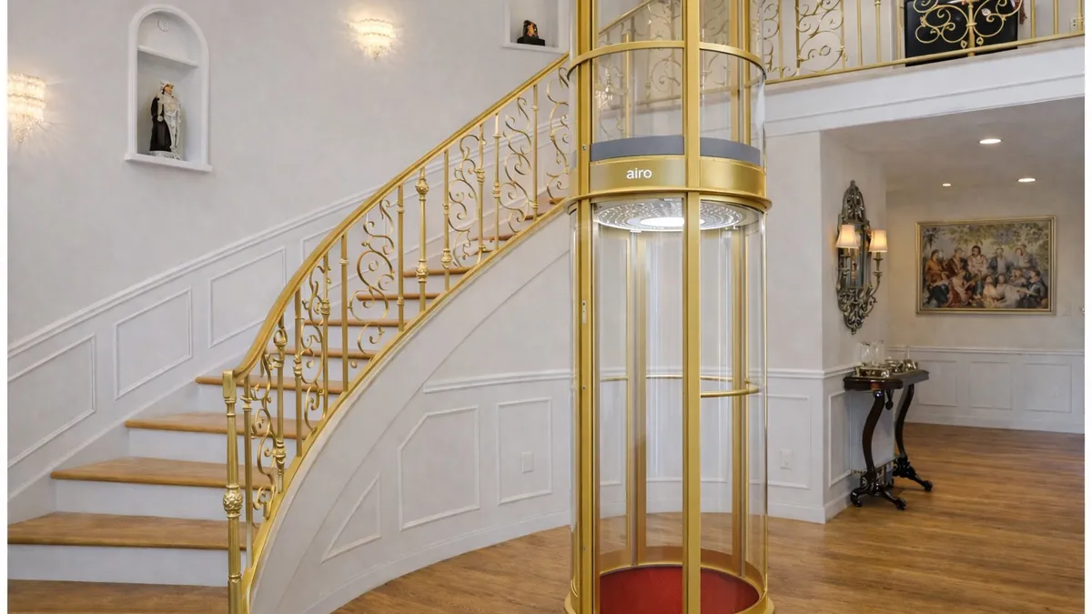 Gold Airo vacuum elevator beside a grand curved staircase in a luxury home